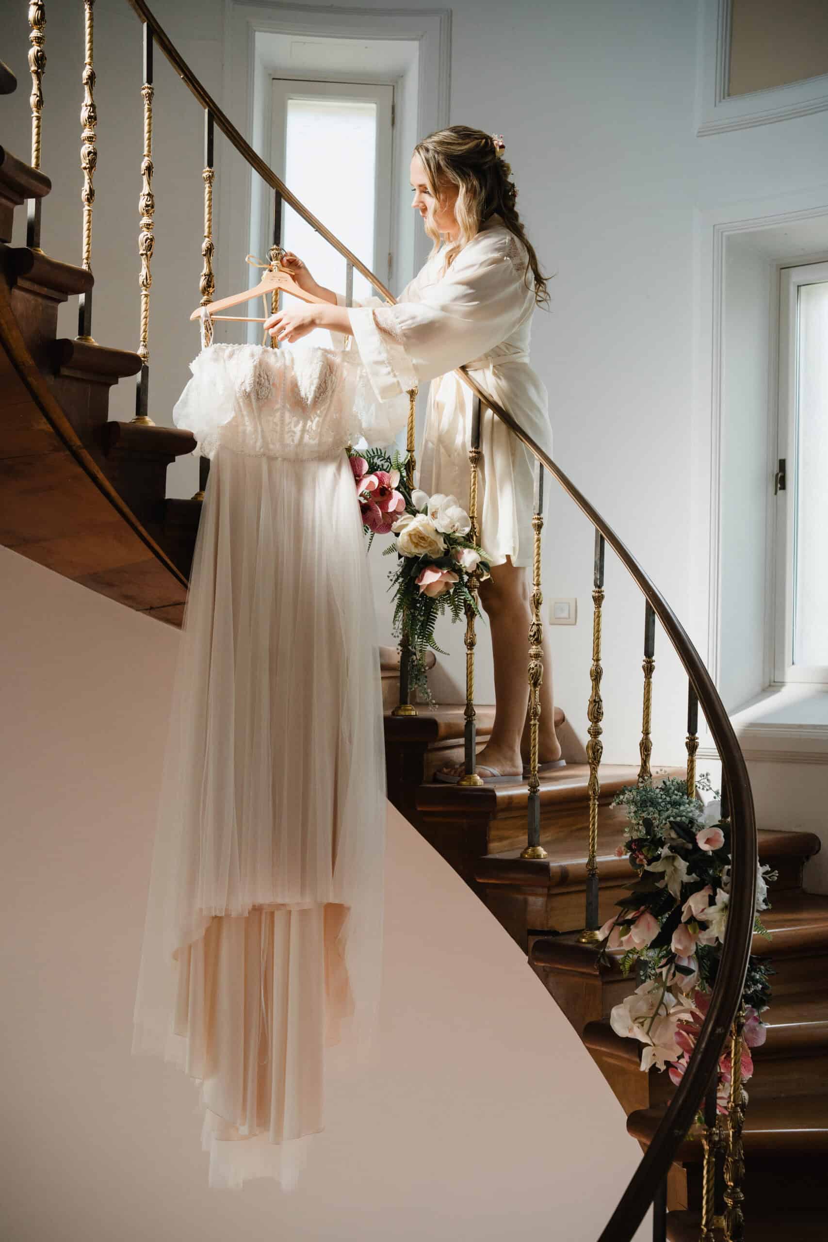 Bride hanging wedding dress on floral staircase by Estudio Zoe