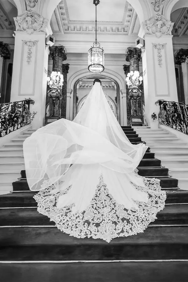 Black-and-white portrait of a bride with a long lace veil on the grand staircase at Casino de Madrid